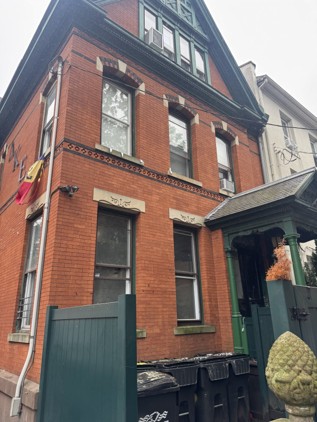 Detail of the second-story windows, showing the segmental-arched brick hoods with stone keystones, the corbelled cornice band, and the carved stone panels below each window.