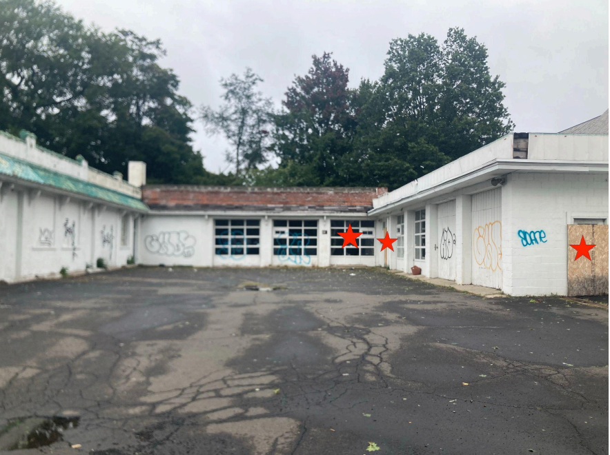 View from parking lot of interior walls of the building. Note that red stars denote broken or boarded up glass doors/windows, as well as the lack of the green awning running around the building as is present in earlier images chronologically.