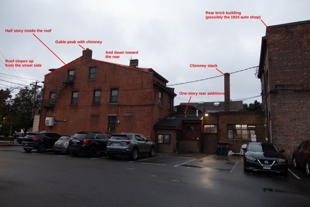 The rear and east side of 155/153 Wooster Street, seen from the parking lot behind the building. A one-story brick and wood-clad service addition with a tall brick chimney stack is visible. Architectural details like the building’s half story and gabled roof are highlighted on the image. 